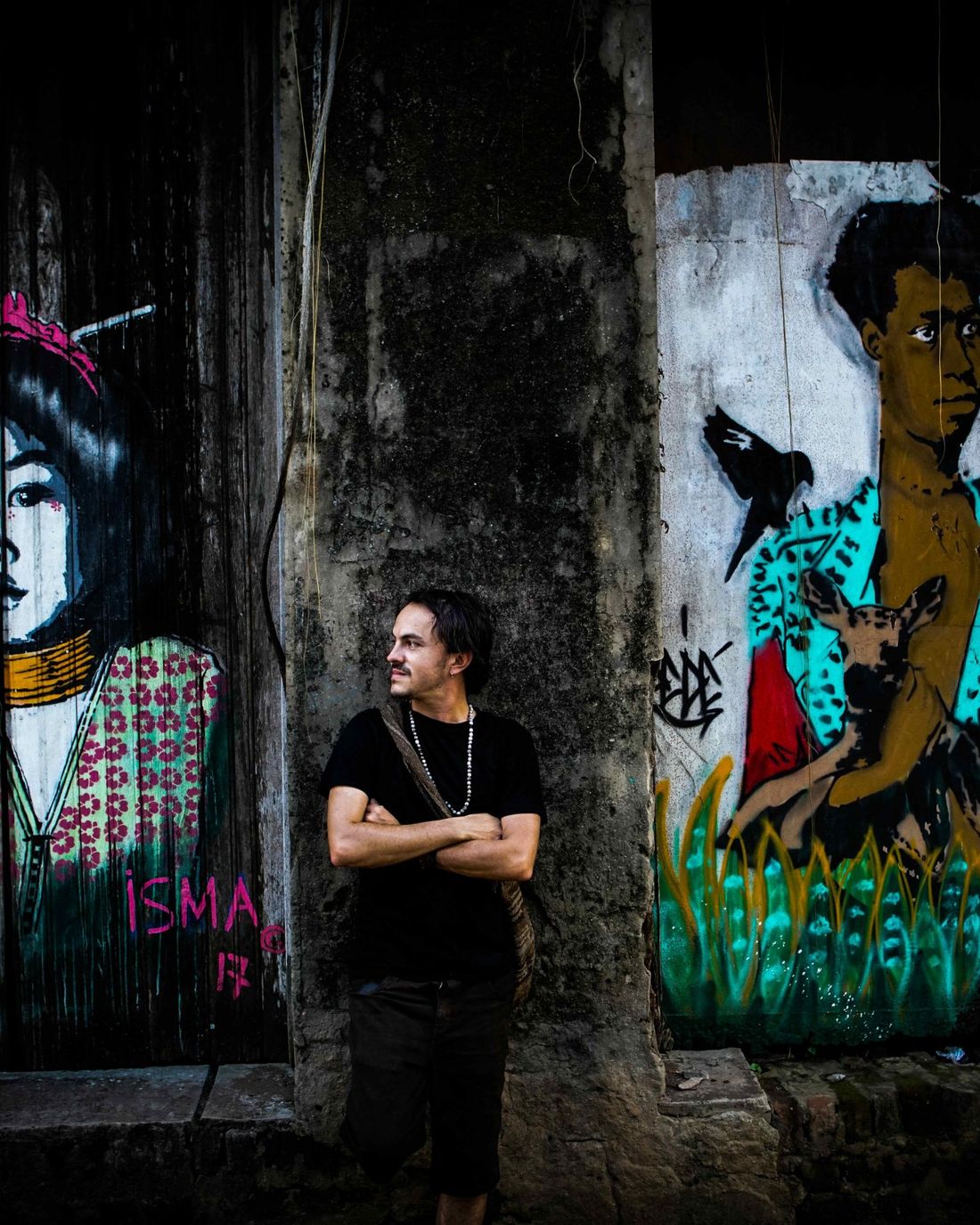 Iván standing with arms crossed between two murals, looking to the side